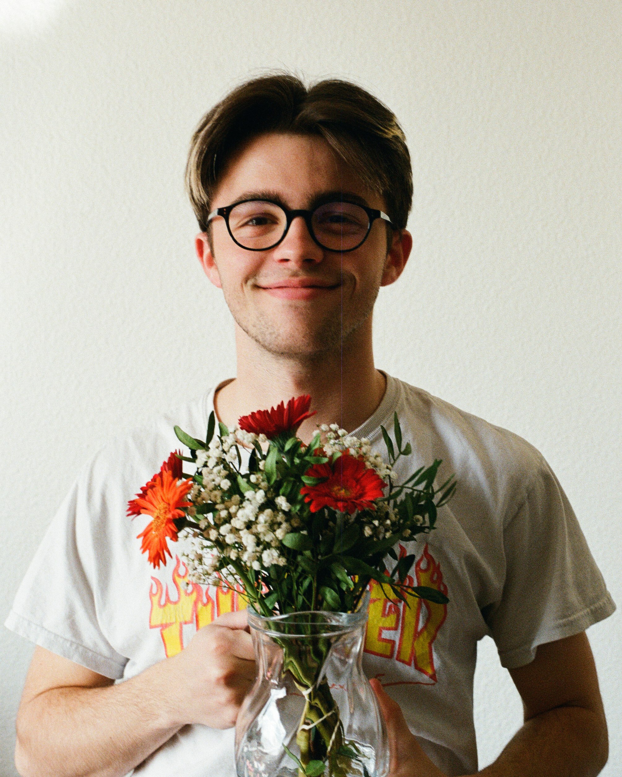 man in white crew neck t-shirt holding bouquet of red flowers